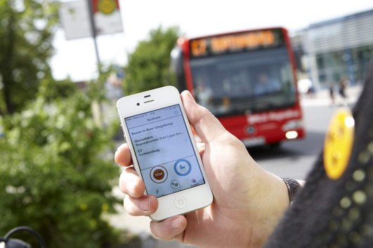 Bild eines Smartphone-Bildschirms mit Bus im Hintergrund. Foto: Beylemans Fotografie