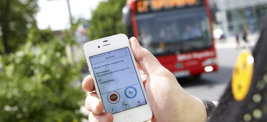 Bild eines Smartphone-Bildschirms mit Bus im Hintergrund. Foto: Beylemans Fotografie
